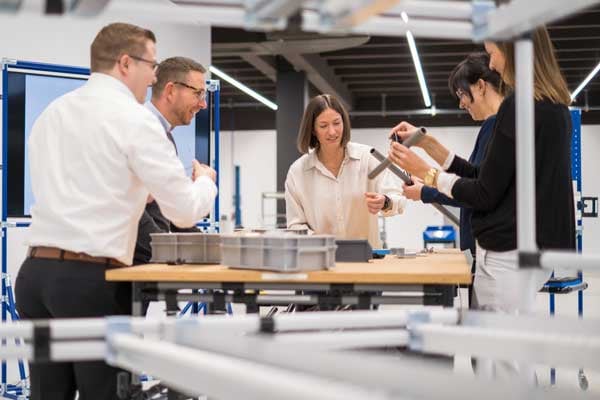 Einige Personen stehen um einen Tisch und halten Komponenten des Rohr Stecksystems in der Hand. 