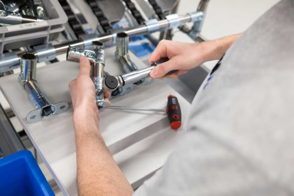At a BeeWaTec assembly workstation, someone assembles something from various components of the pipe racking system