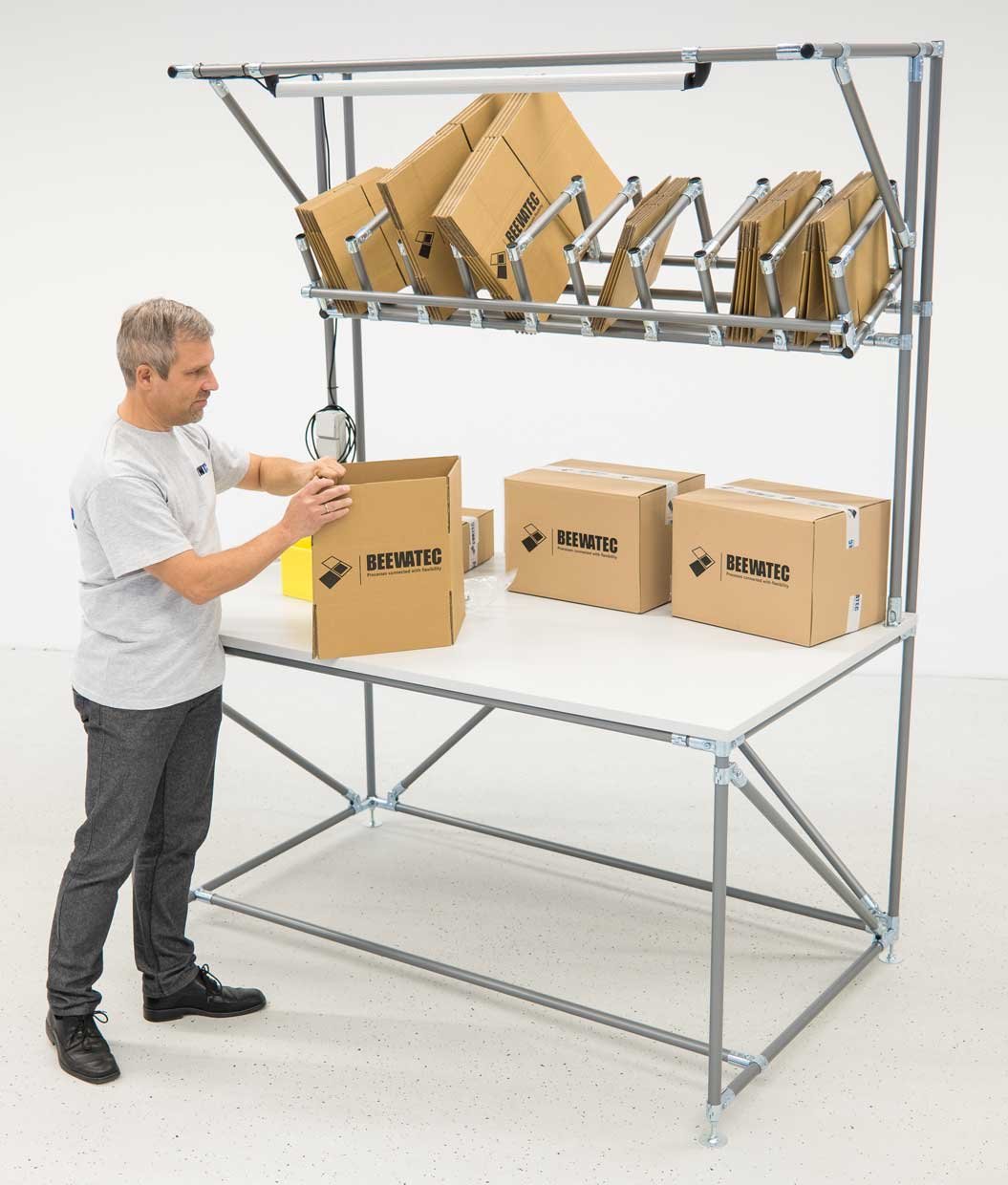 Eine Person verpackt Teile in einen Karton an einem Packtisch von BeeWaTec