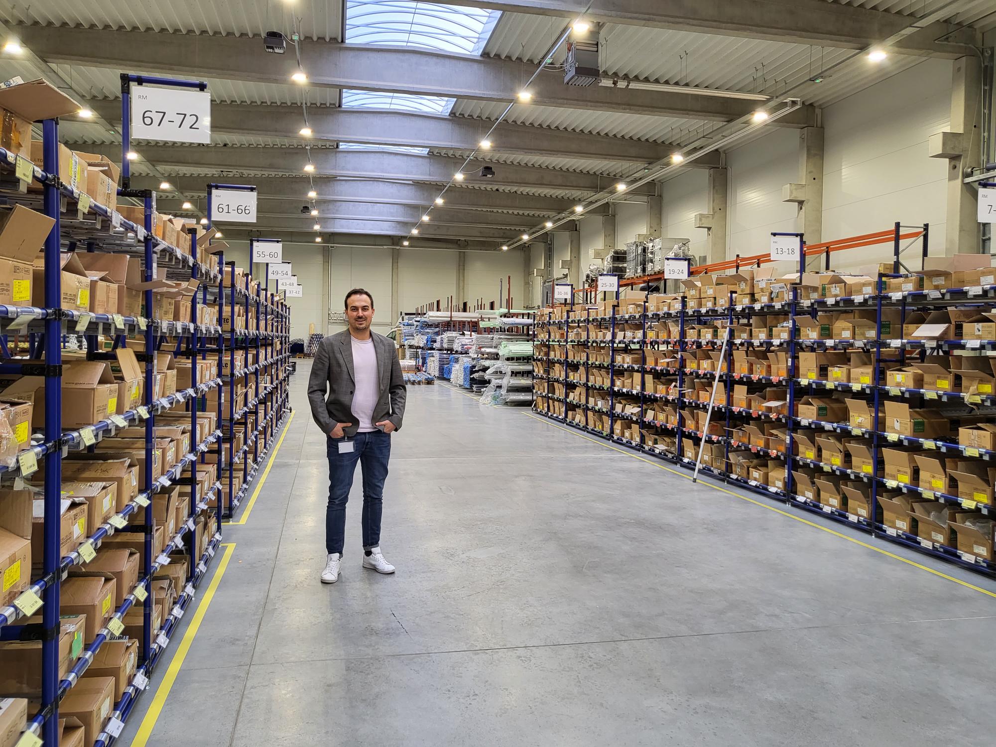 COO Joachim Walter steht in einer großen Lagerhalle zwischen Lagerregalen.