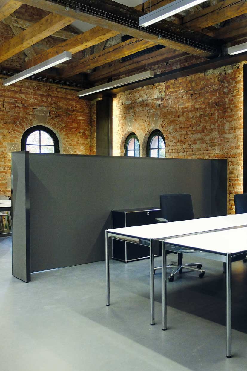 Duża przestrzeń biurowa, w której ścianka działowa pokryta szarą tkaniną oddziela od siebie dwie strefy