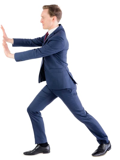 A young man in a suit pushes something invisible aside with both hands.