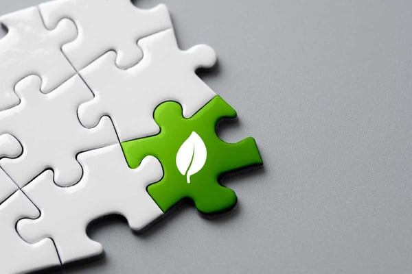 Some connected white puzzle pieces; one puzzle piece is green with a leaf on it